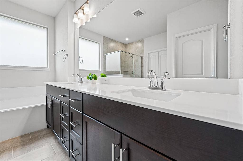 10008 Birchpoint Drive, Fort Worth, TX 76108 Dual undermount sinks with chrome faucets, dark wood-finish cabinetry, white countertop, large wall-mounted mirror, and tile flooring