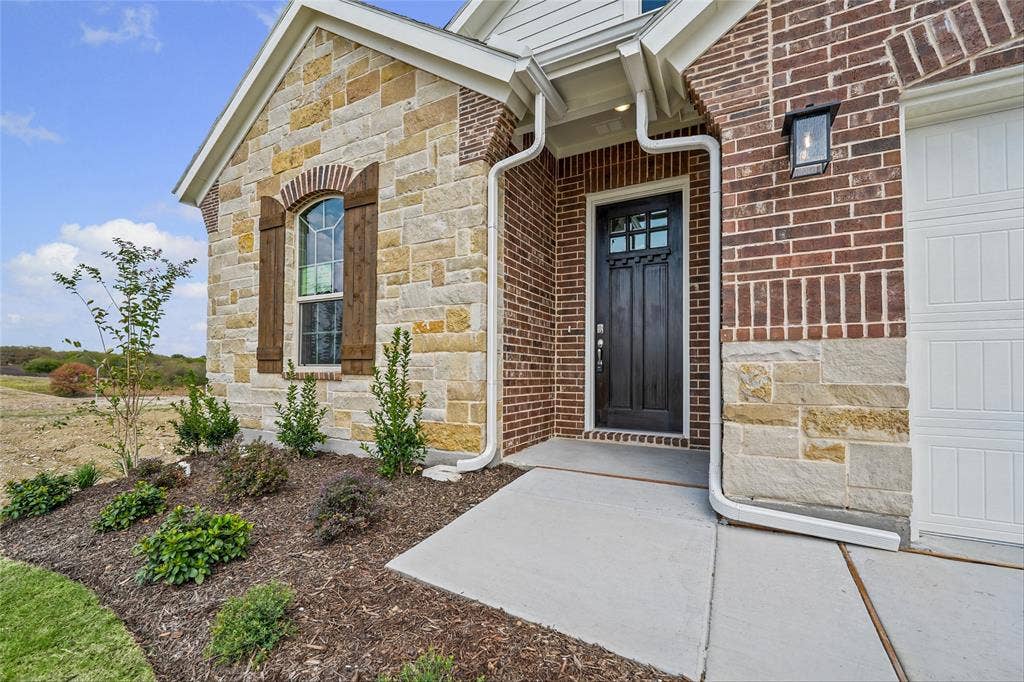 10008 Birchpoint Drive, Fort Worth, TX 76108 Brick and stone exterior with architectural shingles, detailed wood shutters, and an arched window