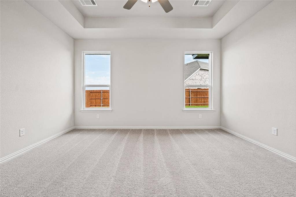 10004 Birchpoint Drive, Fort Worth, TX 76108 Tray ceiling with a ceiling fan, two windows, and light gray carpeting