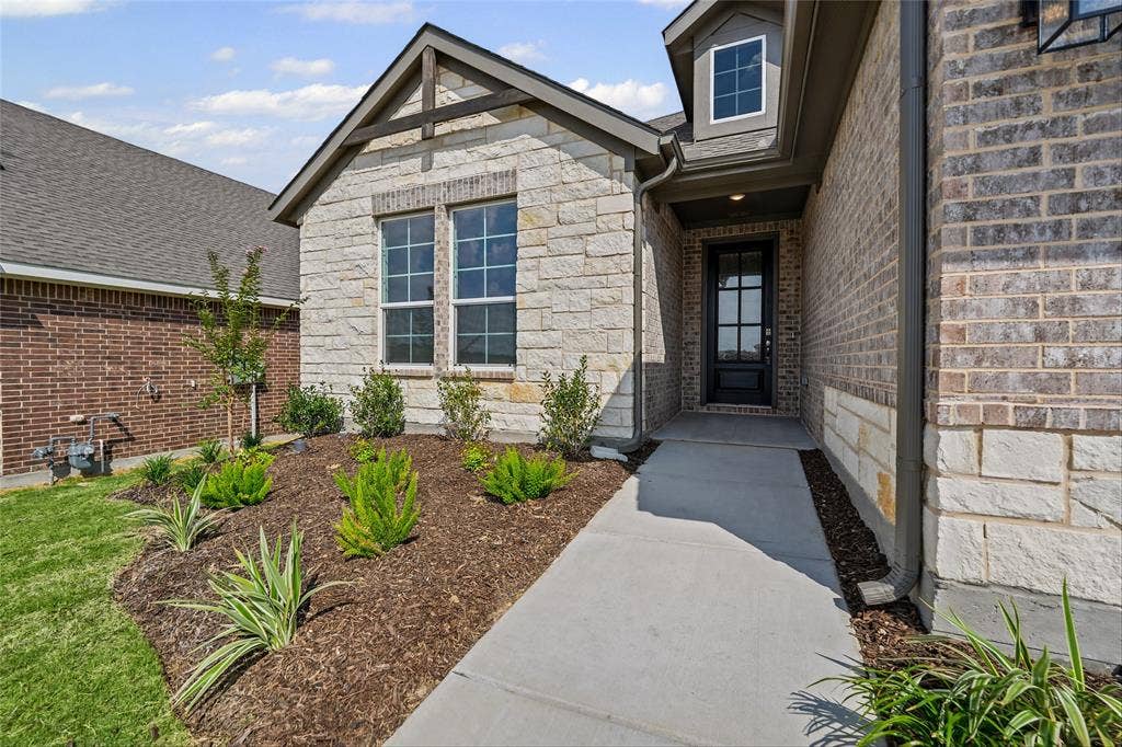 10004 Birchpoint Drive, Fort Worth, TX 76108 Stone and brick exterior with a pitched roofline, decorative gable truss, and a dark paneled entry door with multiple lites