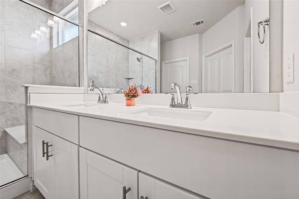 10004 Birchpoint Drive, Fort Worth, TX 76108 Dual vanity with white cabinetry and chrome hardware, white solid surface countertops, undermount sinks, and a walk-in shower with tile surround and glass enclosure