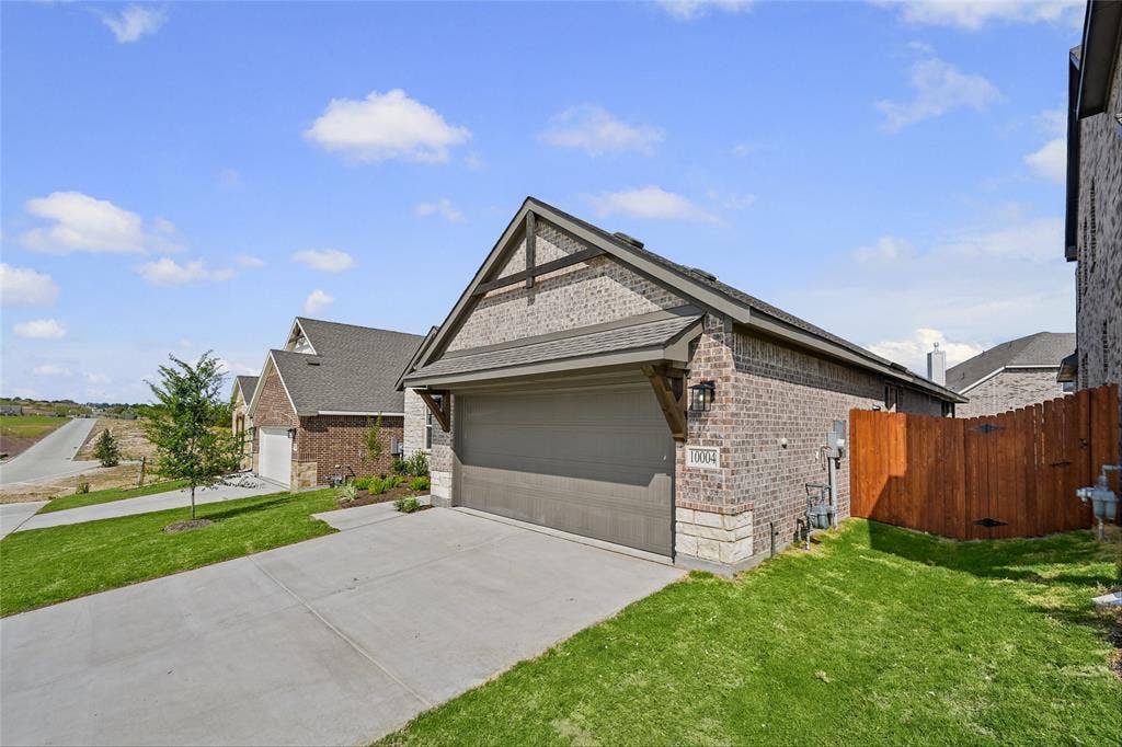 10004 Birchpoint Drive, Fort Worth, TX 76108 Brick and stone exterior with a gabled roofline, attached garage, concrete driveway, and a wood privacy fence