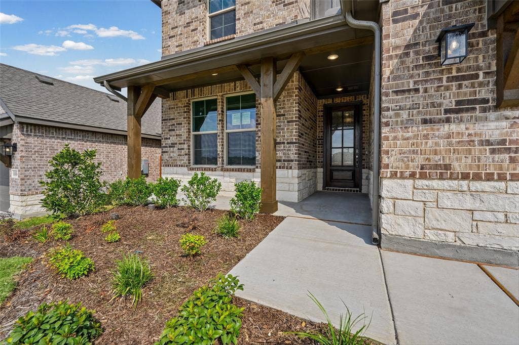 10000 Birchpoint Drive, Fort Worth, TX 76108 Brick and stone exterior featuring a covered entry, wood-finish columns, and a paneled front door with glass inserts