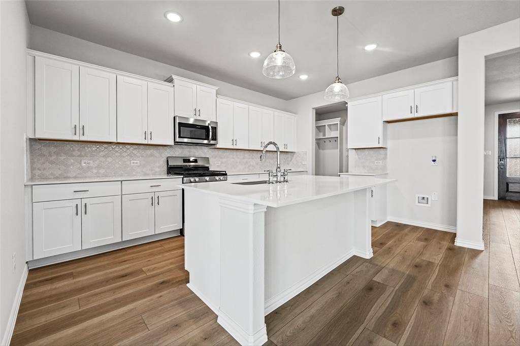 10000 Birchpoint Drive, Fort Worth, TX 76108 Modern kitchen featuring white cabinetry, a central island with a sink, stainless steel appliances, and wood-finish flooring