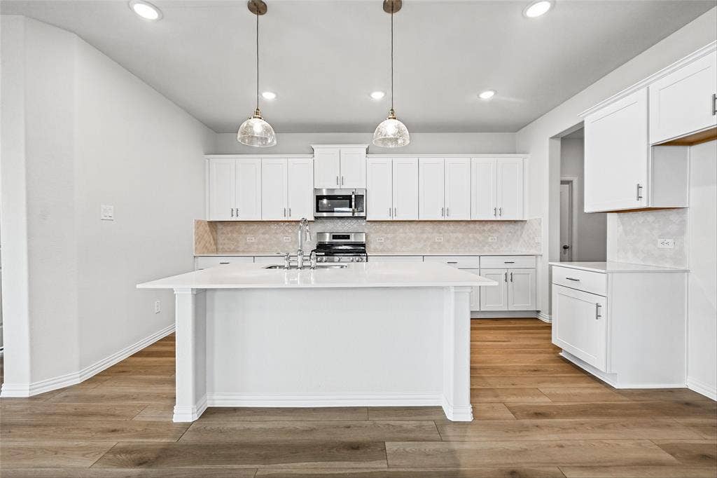10000 Birchpoint Drive, Fort Worth, TX 76108 Kitchen featuring white cabinetry, a central island with a sink, stainless steel appliances, a tile backsplash, and wood-finish flooring