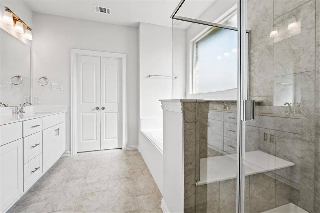 10000 Birchpoint Drive, Fort Worth, TX 76108 Dual vanity with undermount sinks, frameless glass shower enclosure, built-in shower shelving, large soaking tub, and frosted window