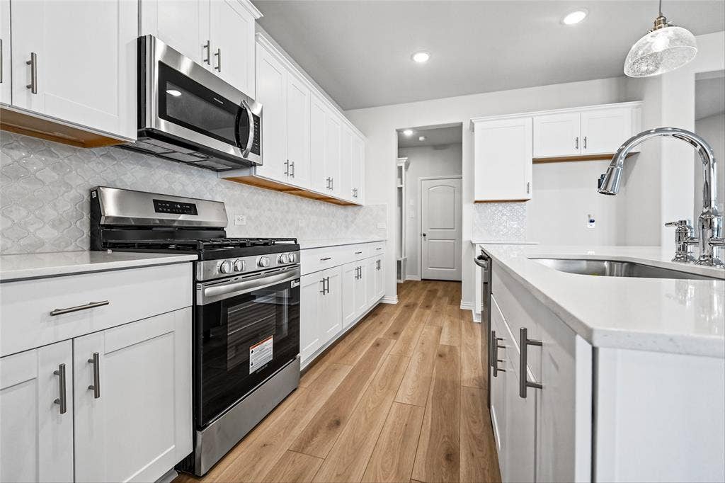 10000 Birchpoint Drive, Fort Worth, TX 76108 White cabinetry, stainless steel appliances, wood-finish flooring, white countertops, and a tile backsplash