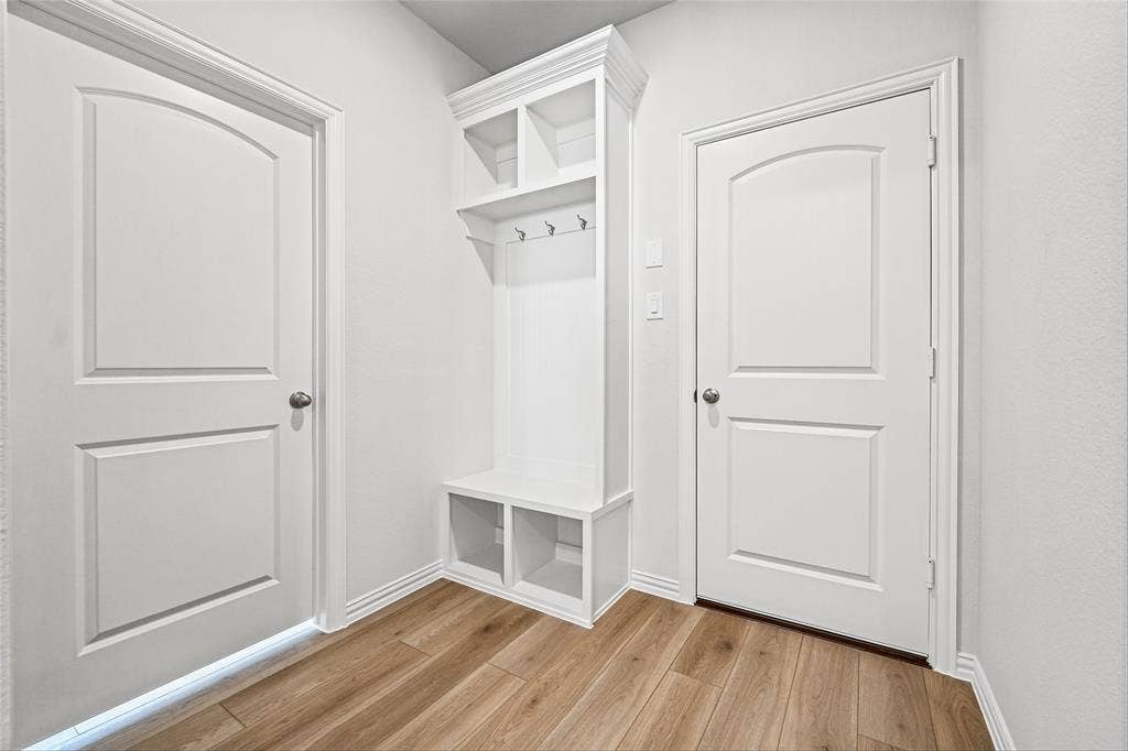 10000 Birchpoint Drive, Fort Worth, TX 76108 Built-in white mudroom bench with storage cubbies and upper shelving, featuring integrated coat hooks and wood-finish flooring