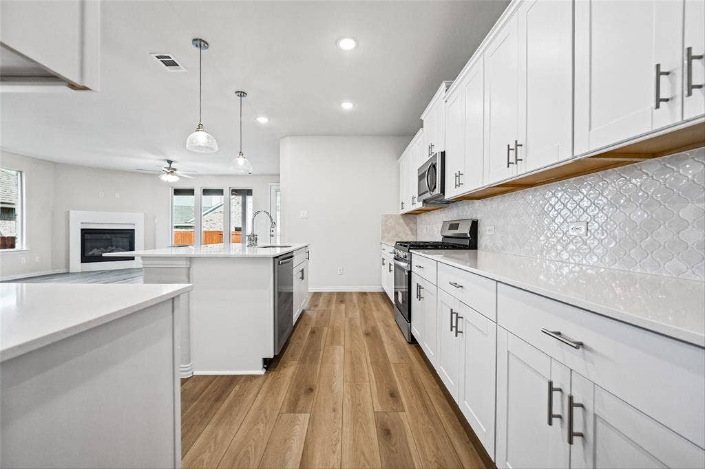 10000 Birchpoint Drive, Fort Worth, TX 76108 Contemporary kitchen featuring white cabinetry, light-toned countertops, a geometric tile backsplash, and wood-finish flooring