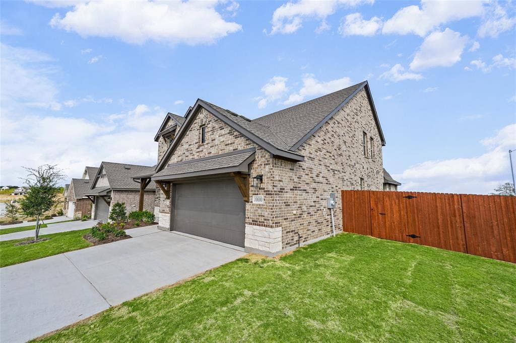 10000 Birchpoint Drive, Fort Worth, TX 76108 Brick exterior with stone accents, a concrete driveway, a wood fence, and a gray asphalt shingle roof