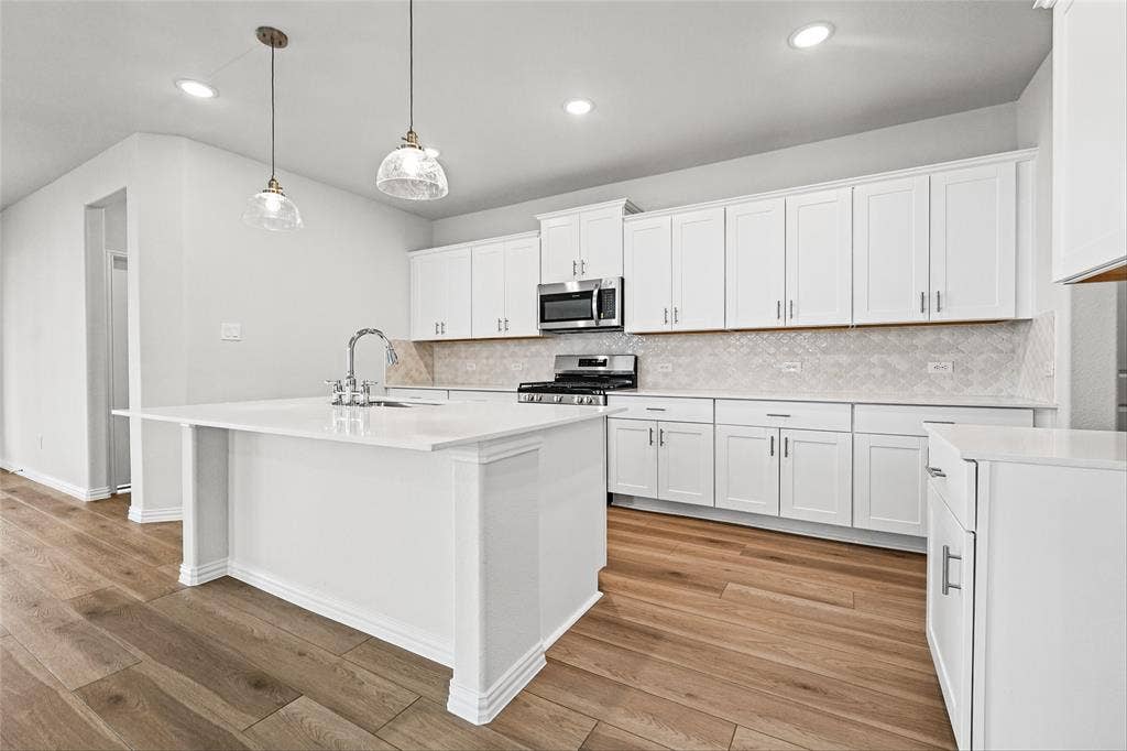 10000 Birchpoint Drive, Fort Worth, TX 76108 Gourmet kitchen featuring a central island with a sink, white cabinetry, integrated stainless steel appliances, a tile backsplash, and wood-finish flooring
