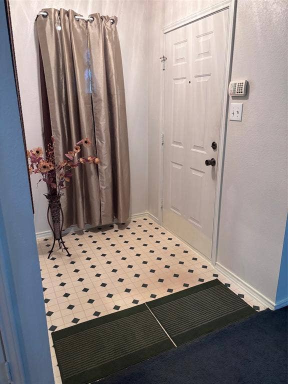 9656 Stonewood Drive, Dallas, TX 75227 Entryway featuring a white paneled door with black hardware, patterned tile flooring, and white baseboards