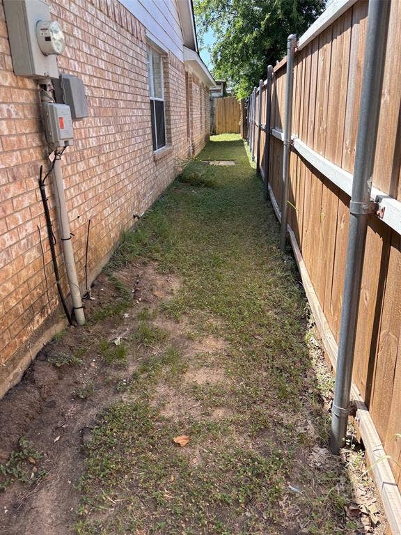 9656 Stonewood Drive, Dallas, TX 75227 Side yard featuring a red brick exterior, multiple windows, a wooden privacy fence, and a grassy path