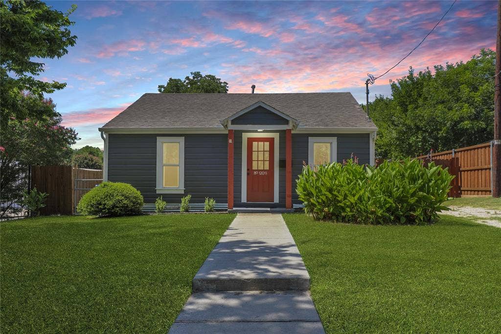1201 1/2 Cole Street, McKinney, TX 75069 Charming single-story home featuring a dark gray exterior, red paneled front door, and a complementary gray roof