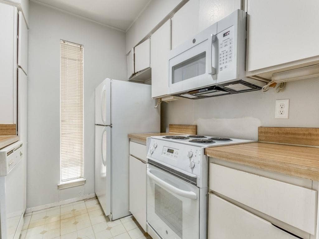 12888 Montfort Drive, #155, Dallas, TX 75230 Kitchen featuring white appliances, upper and lower cabinetry, wood-finish countertops, and a vertical window with blinds