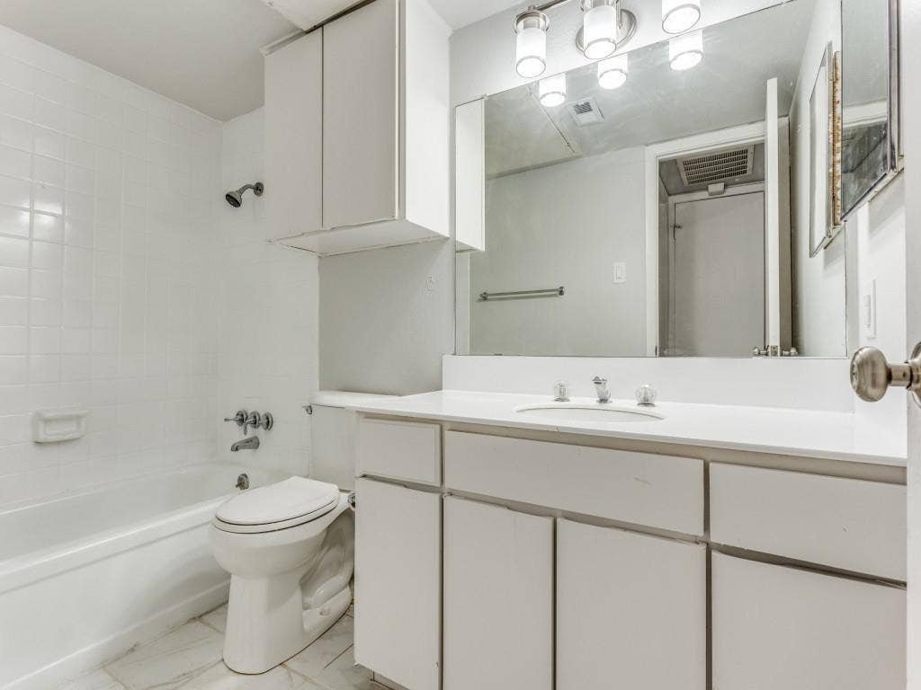 12888 Montfort Drive, #155, Dallas, TX 75230 Bathroom featuring a white vanity with integrated sink, a large mirror, overhead lighting, a tub-shower combination with white tile surround, and built-in white cabinetry
