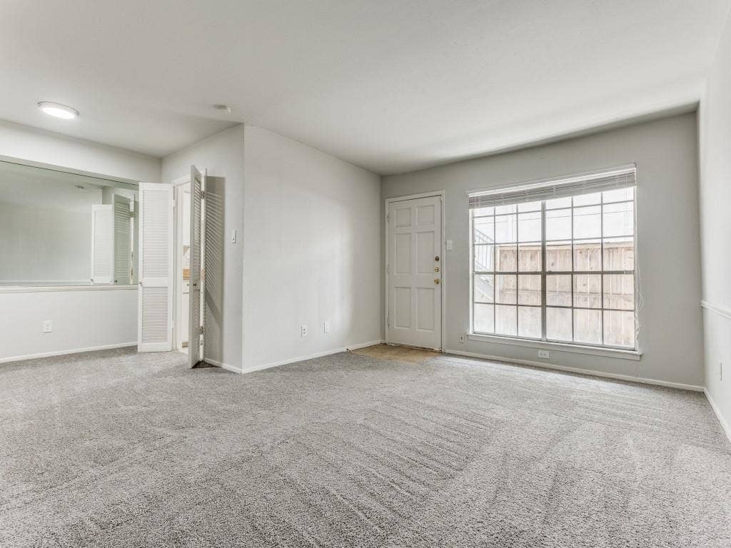 12888 Montfort Drive, #155, Dallas, TX 75230 Spacious living room featuring light gray carpeting, neutral wall finishes, white trim, and a window
