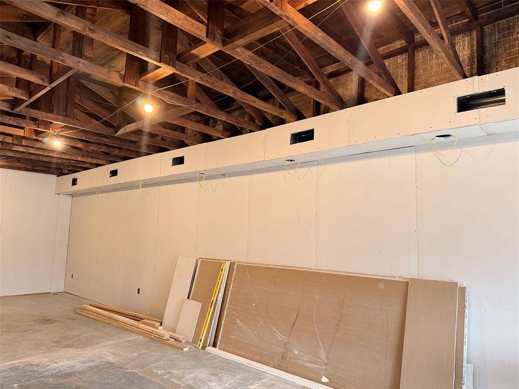 122 W Mccart Street, Krum, TX 76249 Exposed wood beam ceiling with visible brick wall, concrete flooring, and partial drywall installation