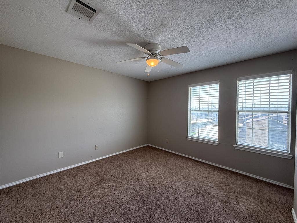 Empty room with plenty of natural light, carpet flooring, a ceiling fan, and a textured ceiling