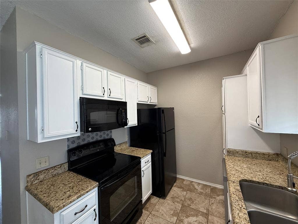 Kitchen with black appliances, white cabinets, and a textured ceiling