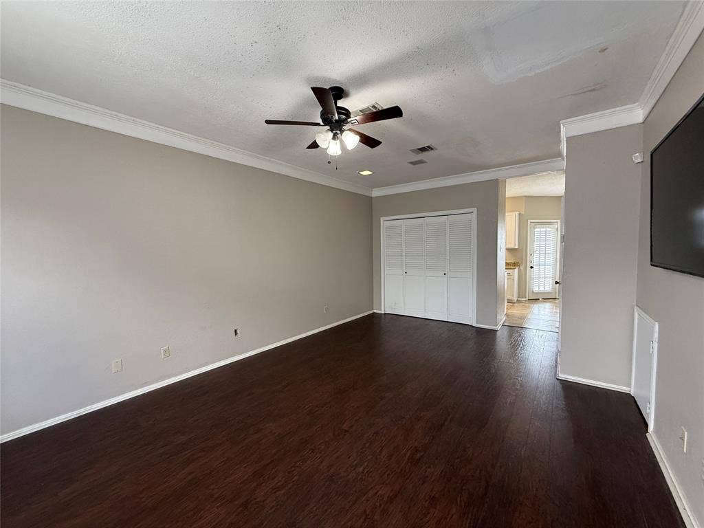Unfurnished bedroom featuring dark wood-style floors, ornamental molding, a textured ceiling, a closet, and a ceiling fan