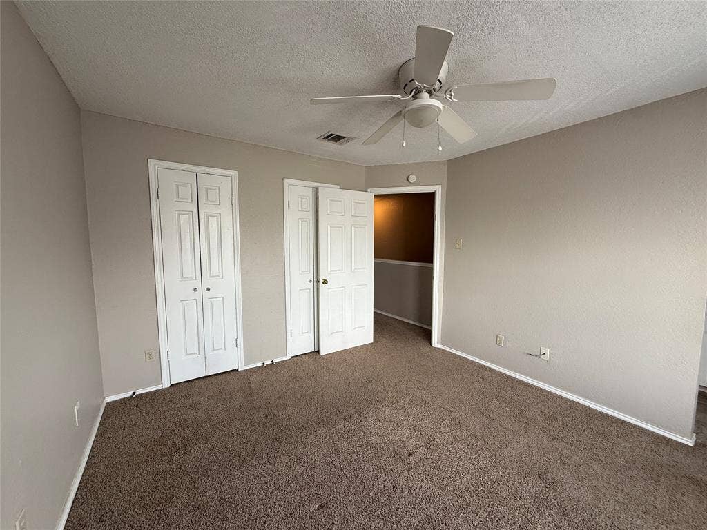 Unfurnished bedroom with carpet flooring, two closets, a textured ceiling, and ceiling fan