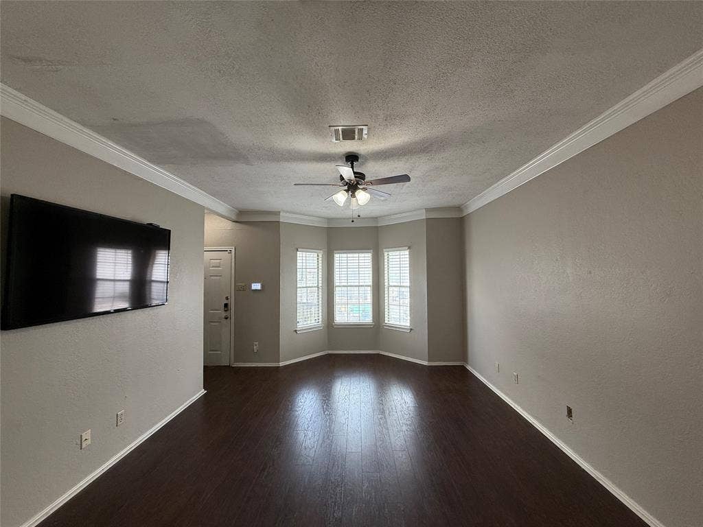 Unfurnished room featuring a ceiling fan, a textured ceiling, ornamental molding, and wood finished floors