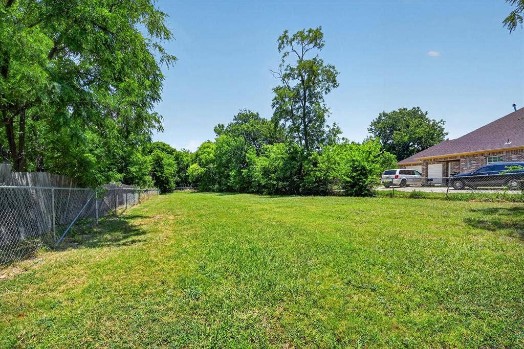4450 Percy Street, Lancaster, TX 75134 Expansive green lawn with mature trees and a chain-link fence bordering the property
