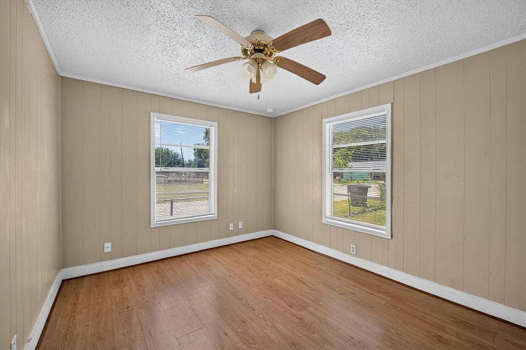 4450 Percy Street, Lancaster, TX 75134 Room featuring wood-finish flooring, two large windows, a ceiling fan with light fixture, and vertical paneling walls