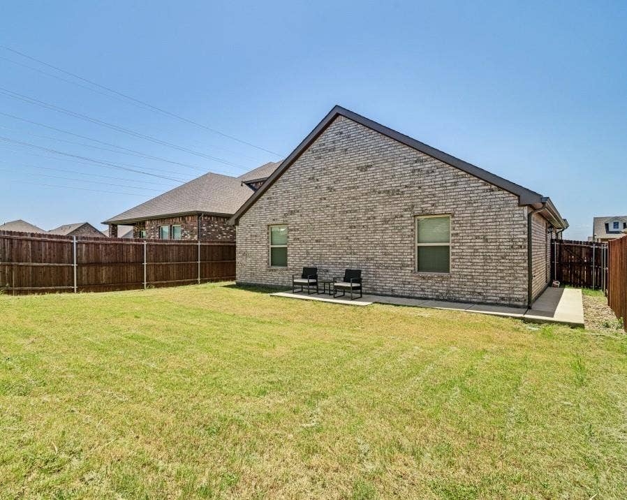 Expansive backyard featuring a manicured lawn, full privacy fencing, a concrete patio, and a brick exterior with dark trim