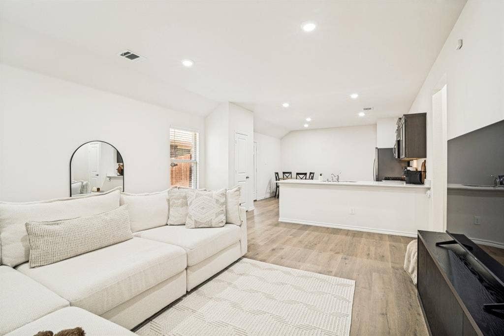 Open-concept living area with wood-finish flooring, recessed lighting, and a kitchen featuring dark cabinetry and a light-toned countertop