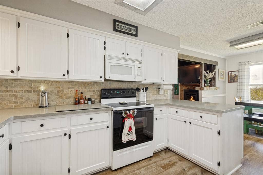 906 Clearview Street, Krum, TX 76249 Kitchen featuring white cabinetry with beadboard paneling, light-toned countertops, stone-look tile backsplash, and LVP flooring