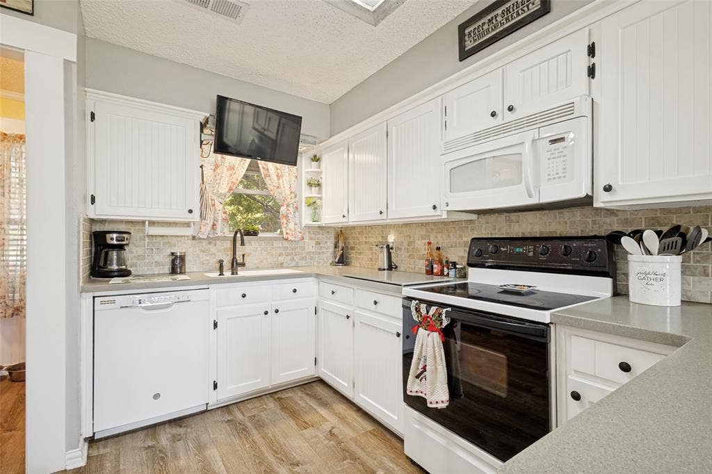 906 Clearview Street, Krum, TX 76249 Kitchen featuring white cabinetry, light-toned countertops, tile backsplash, LVP and a window above the sink
