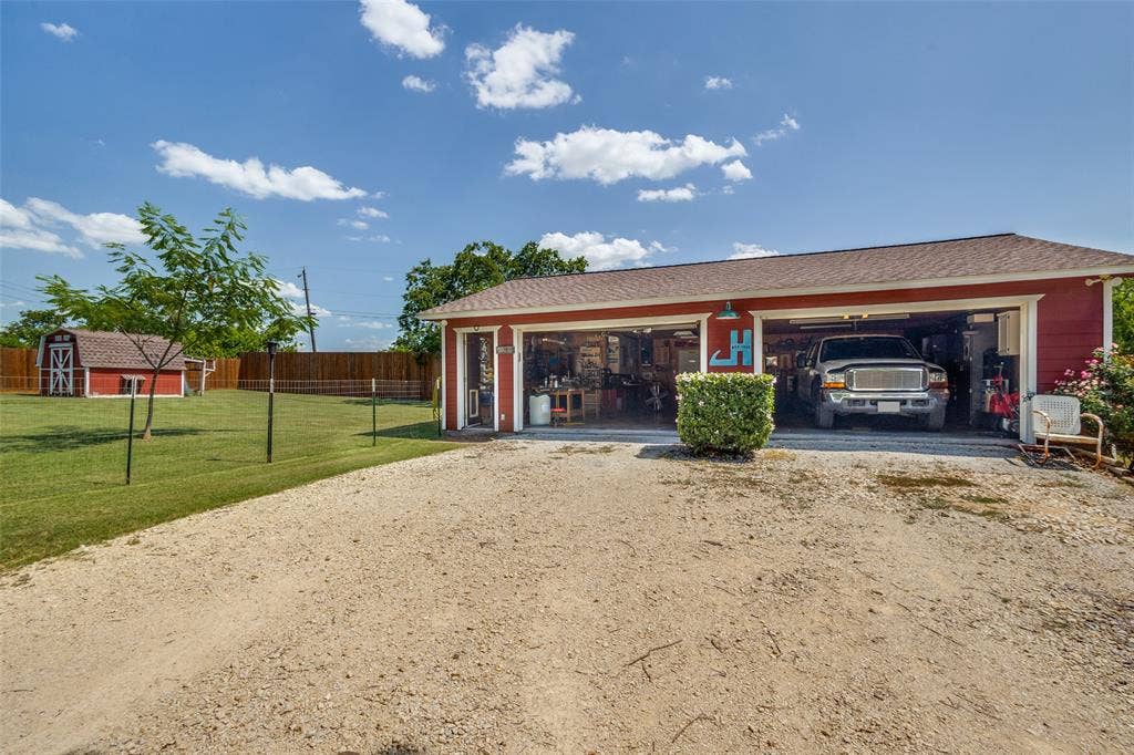 906 Clearview Street, Krum, TX 76249 A two-car garage with overhead doors and workshop and a gravel driveway