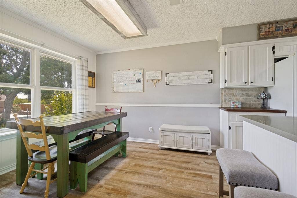 906 Clearview Street, Krum, TX 76249 Bright dining area featuring LVP flooring, a large window, a light gray two-tone wall, white cabinetry with dark hardware.