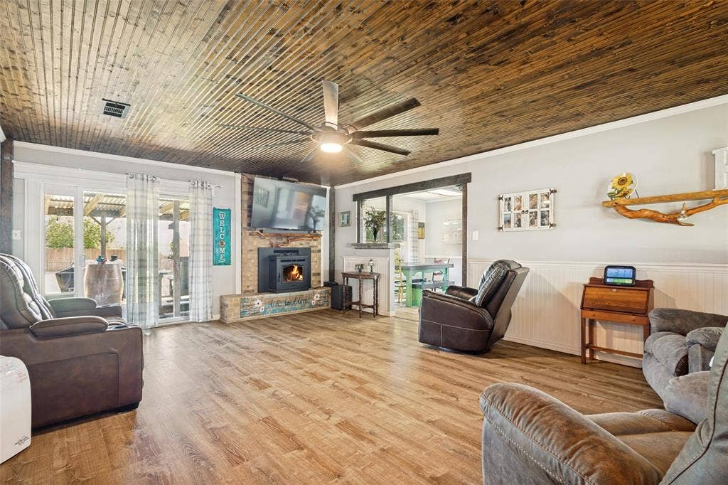 906 Clearview Street, Krum, TX 76249 Spacious living area featuring LVP flooring, a wood plank ceiling, and a brick fireplace with a wood mantel