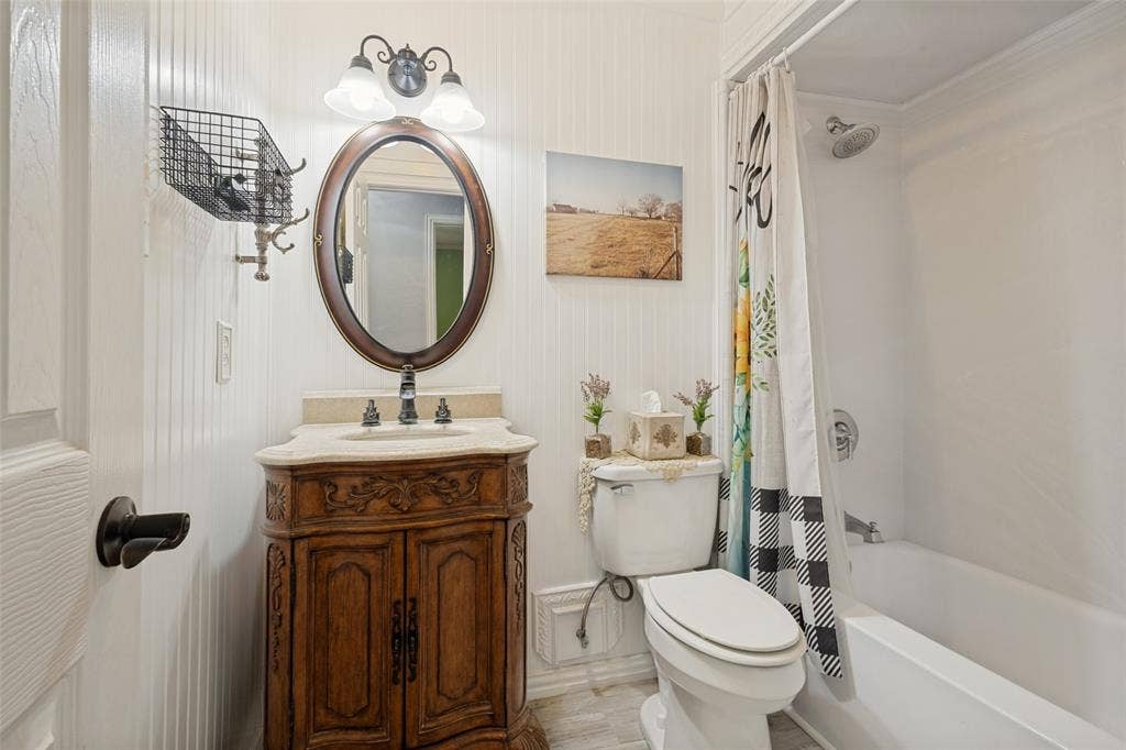 906 Clearview Street, Krum, TX 76249 Bathroom featuring a carved wood vanity with a stone countertop, an oval mirror, and a shower-tub combination.