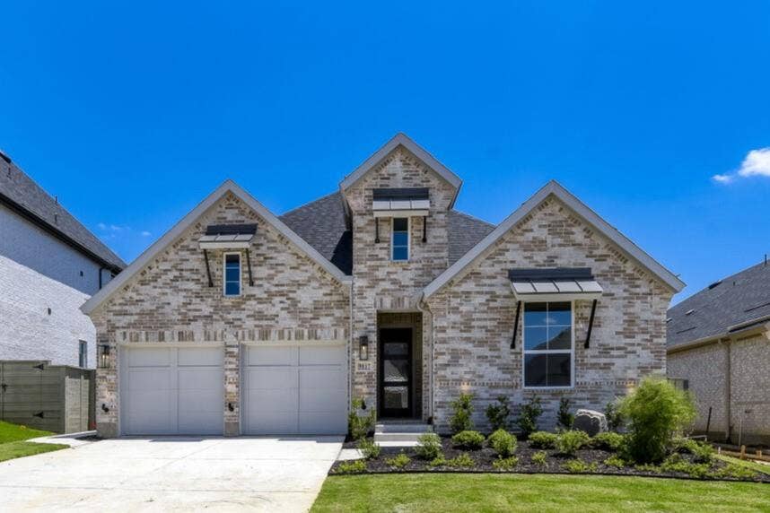 Gabled brick facade with stone accents, integrated two-car garage, contemporary front door, and manicured landscaping