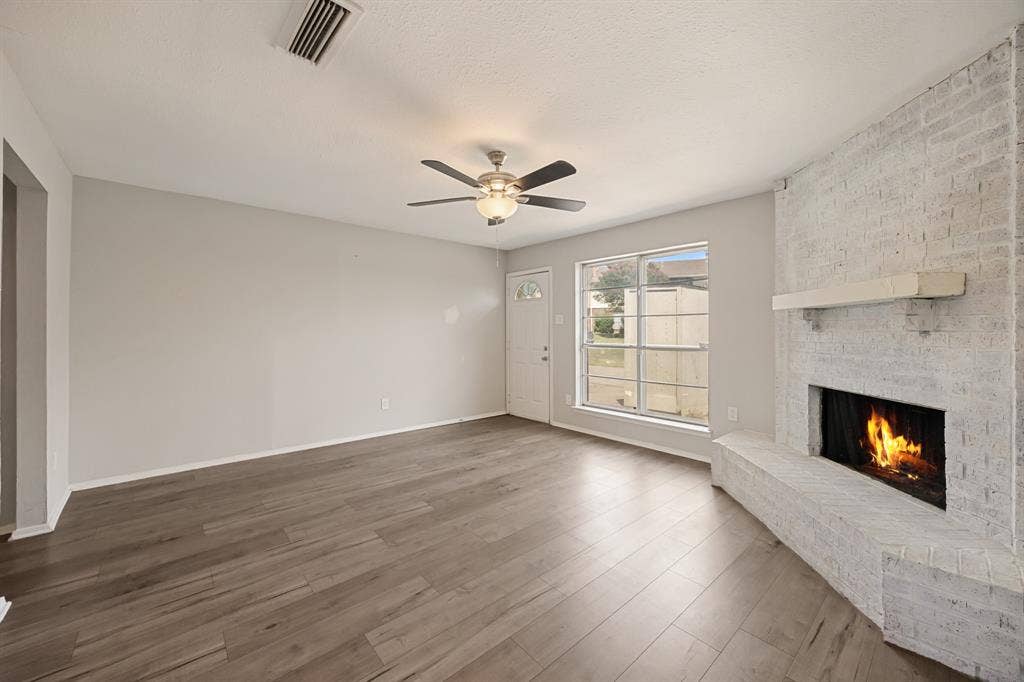 1 E Mountain Lane, #33, Grand Prairie, TX 75052 Spacious living area featuring wood-finish flooring, a white-washed brick fireplace with hearth and mantel, and a ceiling fan with integrated lighting