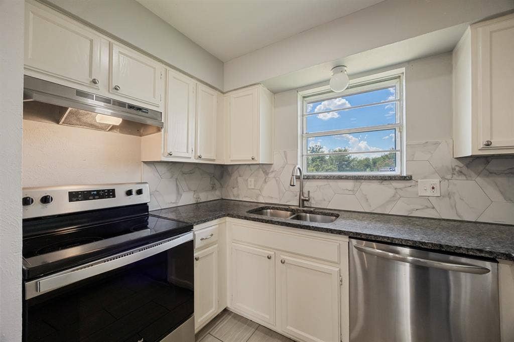 1 E Mountain Lane, #33, Grand Prairie, TX 75052 Kitchen featuring white cabinetry, dark granite countertops, hexagonal tile backsplash, stainless steel appliances, and a window