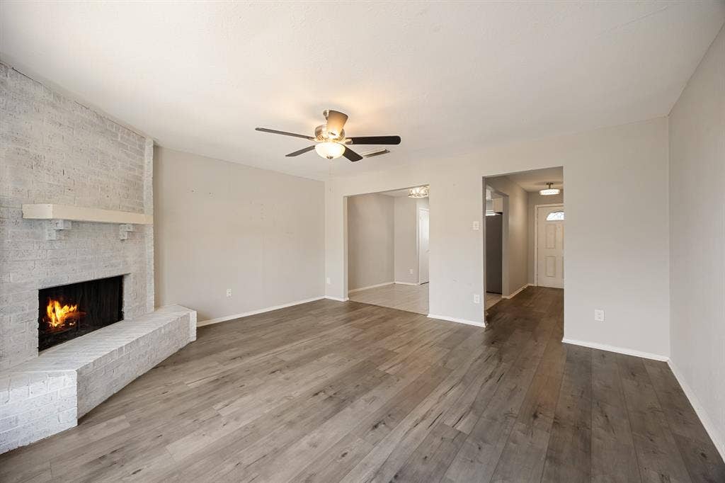1 E Mountain Lane, #33, Grand Prairie, TX 75052 Living area featuring light wood-finish flooring, a painted brick fireplace with a mantle, and a ceiling fan with integrated lighting