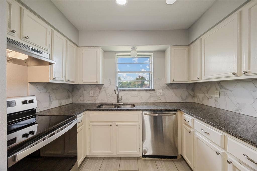 1 E Mountain Lane, #33, Grand Prairie, TX 75052 U-shaped kitchen featuring white cabinetry, dark stone countertops, a tile backsplash with a geometric pattern, and stainless steel appliances