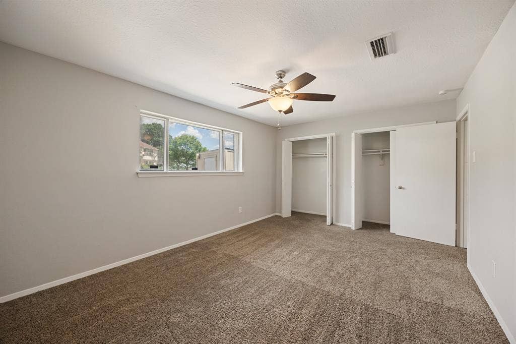 1 E Mountain Lane, #33, Grand Prairie, TX 75052 Carpeted room featuring a ceiling fan with integrated lighting, two closets with bi-fold doors, and a multi-pane window