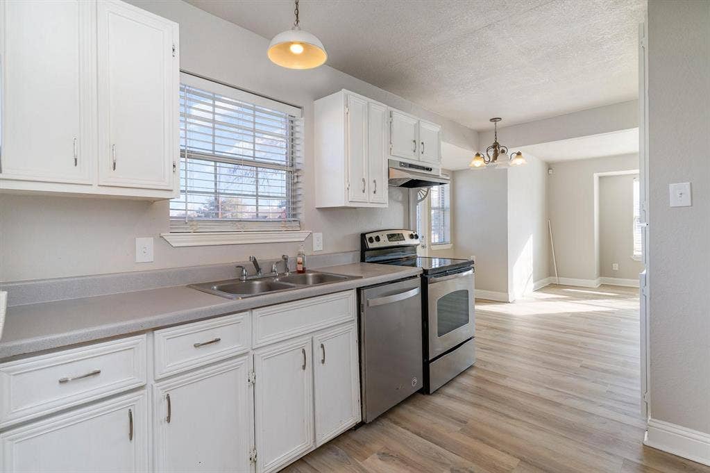 500 S Ballard Avenue, Wylie, TX 75098 Kitchen featuring white cabinetry with silver-tone hardware, a double basin stainless steel sink, light grey countertops, and stainless steel appliances including a range and dishwasher