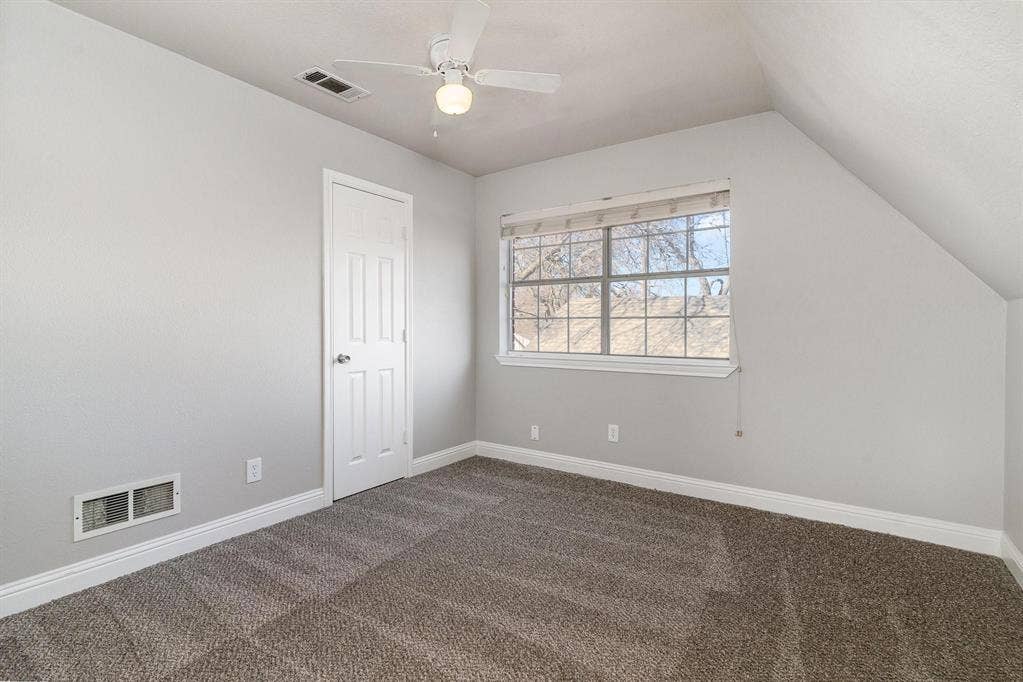 500 S Ballard Avenue, Wylie, TX 75098 Room featuring neutral gray wall paint, textured carpeting, a multi-pane window with blinds, and an angled ceiling