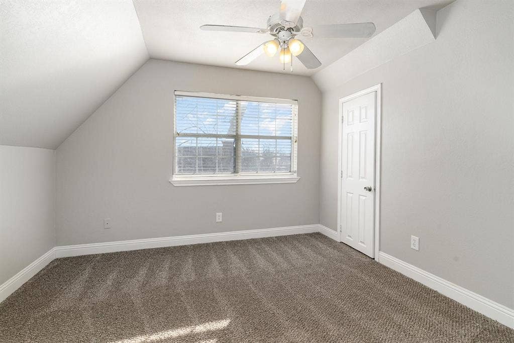 500 S Ballard Avenue, Wylie, TX 75098 Carpeted room featuring a window with blinds, a white ceiling fan with integrated lighting, a paneled door, and angled ceilings