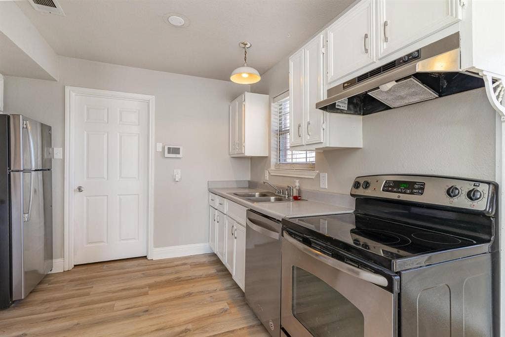 500 S Ballard Avenue, Wylie, TX 75098 Kitchen featuring stainless steel appliances, wood-finish flooring, white cabinetry, light-toned countertops, and a window with blinds