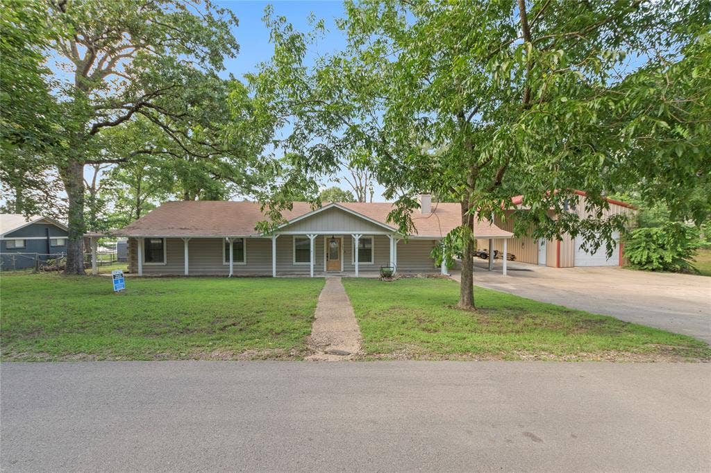 323 Dyer Circle, Payne Springs, TX 75156 Ranch-style residence featuring a covered front porch, a paved driveway, and a detached structure with multiple garage doors