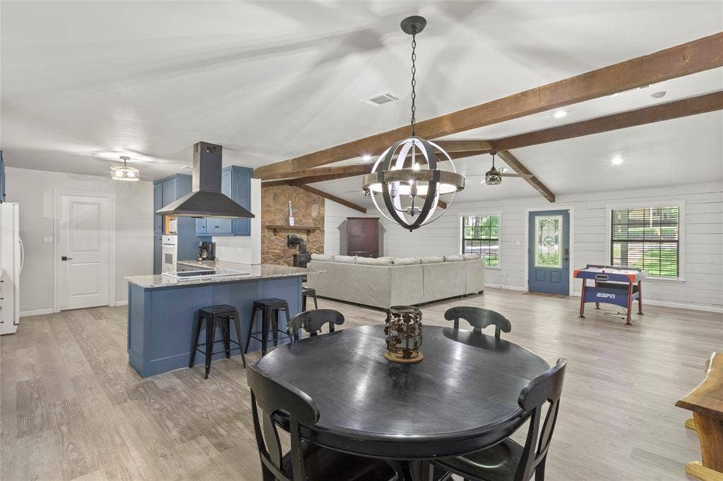 323 Dyer Circle, Payne Springs, TX 75156 Open-concept living space with vaulted ceilings, exposed wood beams, wood-finish flooring, a kitchen island with stone countertop, and a stone accent wall