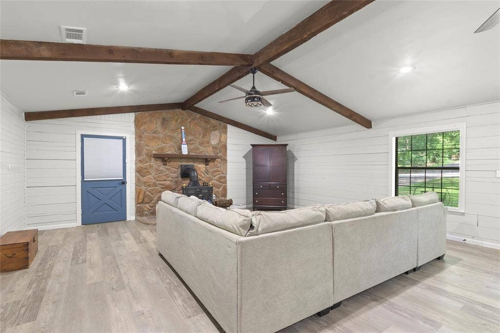 323 Dyer Circle, Payne Springs, TX 75156 Vaulted ceiling with exposed wood beams, shiplap walls, stone-clad fireplace, wood-finish flooring, and a blue Dutch door